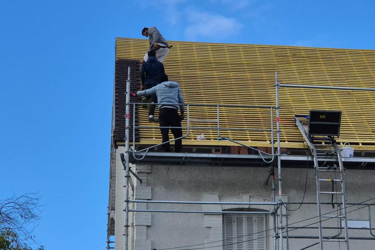 Trois couvreurs de l'équipe posant l'écran sous toiture et les liteaux d'une maison, sous échafaudage