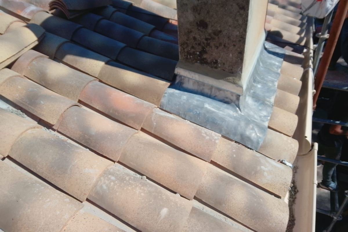 Solin en zinc neuf façonné autour d'une souche de cheminée, sur une couverture en tuiles